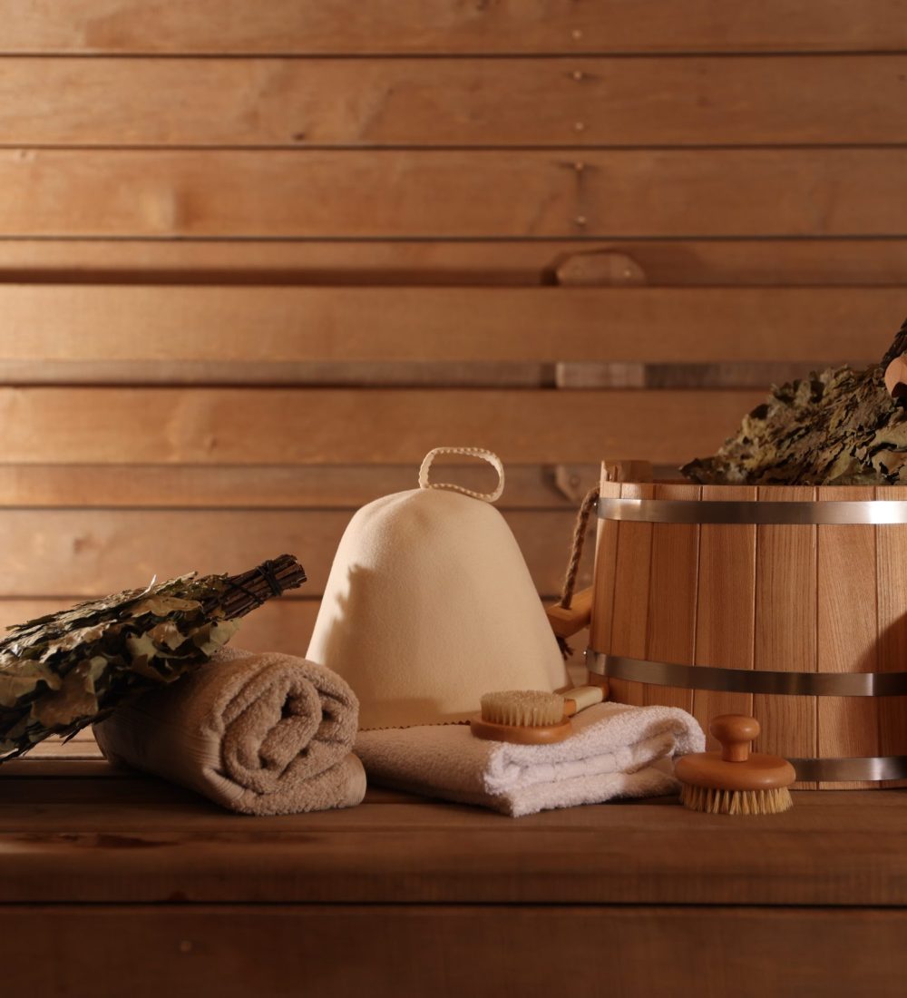 Bucket, whisks, massaging brushes and other equipment on wooden bench in sauna